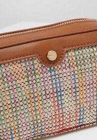 Petite pochette zippée bordée de cuir marron avec un bouton doré et un tissu tissé multicolore présentant un motif rayé vertical.