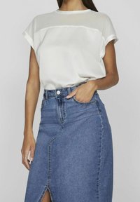 Vit blus med ett genomskinligt överdel, korta ärmar, i kombination med en ljusblå denimkjol med en framklippning och synliga sömmar.