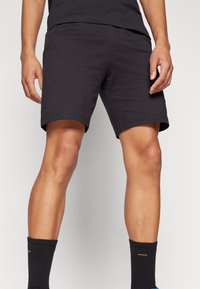 Pantalones cortos de mezcla de algodón negros con un corte relajado, que presentan un patrón liso, y combinados con calcetas negras acanaladas para mayor comodidad.