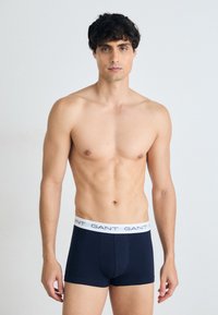 Navyblaue Baumwollboxershorts mit einem weißen Bund, der das "GANT"-Logo trägt. Eng anliegendes Design, glatte Textur und mittellange Beinlänge.