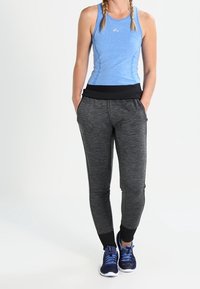 Niebieski bezrękawnik o dopasowanym kroju, zestawiony z czarnymi, tapered spodniami dresowymi z teksturowanym szarym wzorem i elastycznymi mankietami, noszonymi z niebieskimi butami sportowymi.