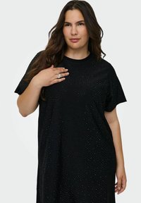 Melna T-krekls ar īsām piedurknēm, kuru rotā punkts raksts visā virsmā un brīvs piegriezums. Mīksta audums, apaļš kakla izgriezums un maigs spīdums.