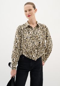 Beige, fekete és barna leopárdmintás blúz, galléros nyakkal és hosszú ujjal, fekete, magasan derekú farmernadrággal párosítva.