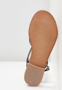 Sandale noire avec un dessus en cuir texturé et une semelle lisse marron. Présente un accent en boucle et un logo embossé sur la semelle intérieure. Taille 37.