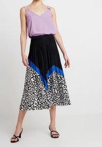Top viola senza maniche con spalline sottili abbinato a una gonna plissettata nera con stampa leopardata bianca e nera e accenti diagonali blu.