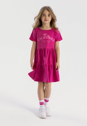 Robe en coton rose à manches courtes, design à volants, col rond, et un motif "California" sur le devant. Baskets blanches et chaussettes rayées.