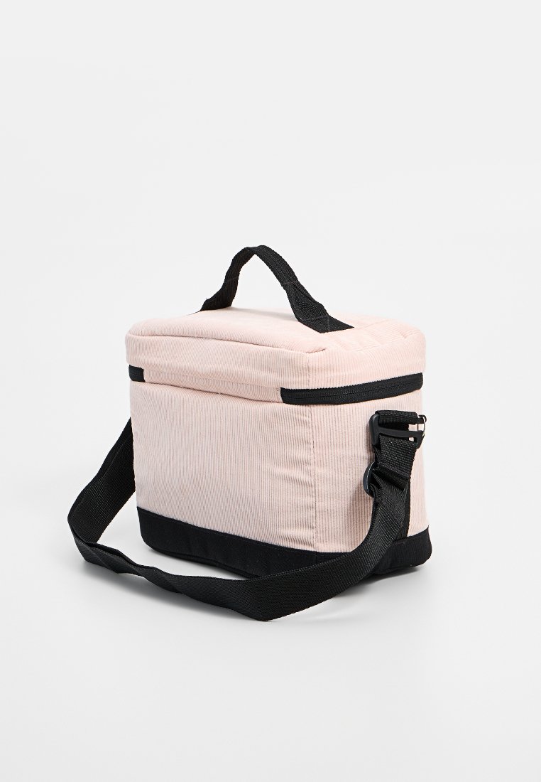 Bolsa aislante de pana rosa con base negra, asa superior y correa ajustable. Presenta un cierre con cremallera y una textura acolchada en la tapa.