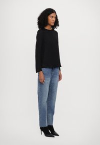 Svart langermet topp med teksturert design, kombinert med lyseblå rett ben jeans og svarte spisse hæler.