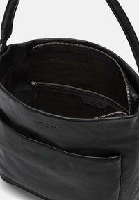 Czarna skórzana torebka o gładkiej fakturze, z zamykaną na suwak kieszenią i detalem z logo. Wnętrze wyłożone tkaniną, wyposażone w wiele przegródek.