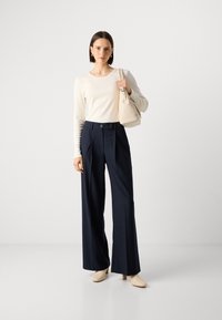 Kremfarget langermet topp, marineblå striper vide bukser, beige veske, og lyse hæler. Glatte teksturer og skreddersydd design.