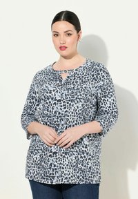 Bluzka w panterkę w odcieniach niebieskiego i czarnego. Posiada rękawy o długości trzy czwarte oraz dekolt w kształcie łezki. Wykonana z miękkiego materiału o luźnym kroju.