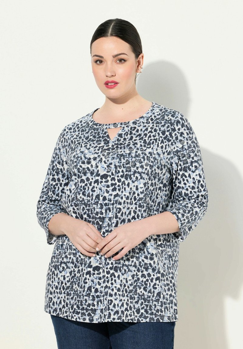 Bluzka w panterkę w odcieniach niebieskiego i czarnego. Posiada rękawy o długości trzy czwarte oraz dekolt w kształcie łezki. Wykonana z miękkiego materiału o luźnym kroju.
