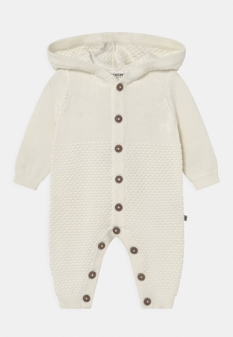 Romper de punto en crema con capucha, cierre de botón marrón, yugo texturizado y puños de canalé. Tejido suave y cálido diseñado para bebés.