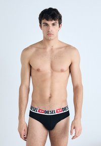 Caleçons noirs avec une ceinture de marque blanche et rouge. Le tissu semble lisse sans motifs visibles. Le modèle se tient droit, face à l'avant.