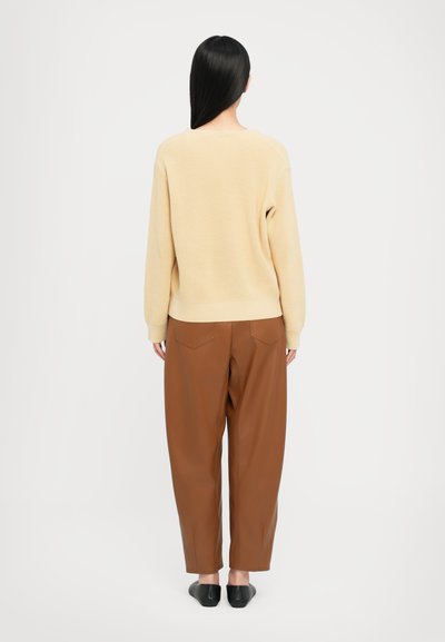 Suéter beige em malha com um corte descontraído, combinado com calças castanhas de cintura alta e estreitas. Sapatos planos pretos completam o visual.