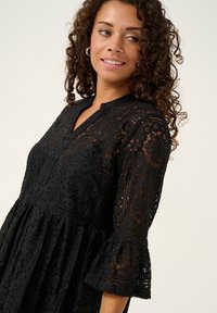 Black lace dress featuring a flared sleeve design, intricate patterns, and a V-neckline. The fabric has a delicate, textured appearance.