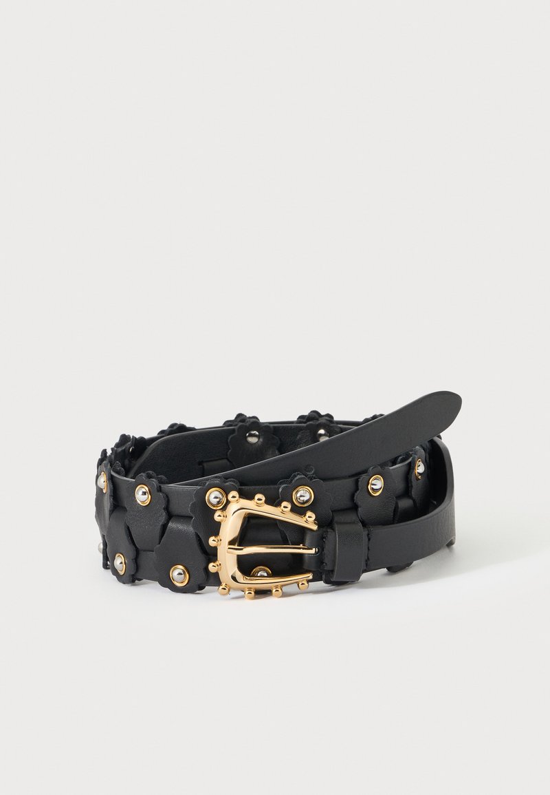 Ceinture en cuir noir avec de petites découpes en forme de fleur, des clous dorés et une boucle décorative dorée avec des clous arrondis, enroulée sur une surface blanche.