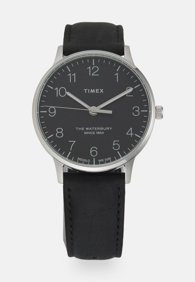 Timex Waterbury sat s crnim brojčanikom, slučajem od srebrnog nehrđajućeg čelika i crnim kožnim remenom. Značajke uključuju numeričke oznake sati i prikaz datuma.