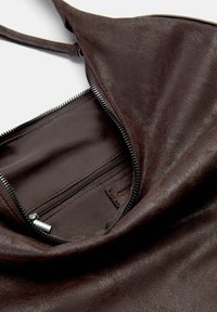 Braune Ledertasche mit glatter Textur, offener Reißverschlussöffnung und einer Innentasche mit kontrastierender Stoffauskleidung.