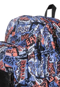 Mochila con una tela estampada que presenta texto estilo graffiti en azul, negro y rojo. Bolsillos con cremallera y herrajes negros, con una superficie texturizada.