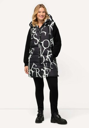 Gevoerde vest met een zwart-wit letterprint, voorzien van een capuchon en contrasterende zwarte gebreide mouwen. Ongeopend met zijzakken, gedragen over zwarte broek.