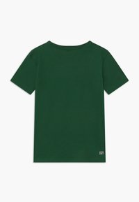 T-shirt en coton vert foncé à manches courtes, col rond, avec une étiquette en bas à droite indiquant "ULTRA DRY". Texture lisse.