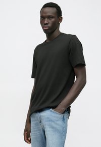 Černé bavlněné tričko s kulatým výstřihem a krátkými rukávy, kombinované se světle modrými džínami. Jednoduchý design bez viditelných vzorů nebo akcentů.