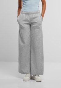 Grå vide joggebukser med elastisk midje, sidelommer og lett tekstur; parret med hvite sneakers.