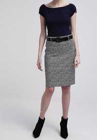 Navyfärgad snäv topp med korta ärmar och ett svart bälte; mönstrad knälång svart och vit peniskjol; svarta ankelstövlar.