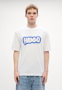 Hvid bomulds t-shirt med et blåt grafisk "HUGO" design i en stiliseret, boble-lignende skrifttype. Løs pasform med korte ærmer og rund halsudskæring.