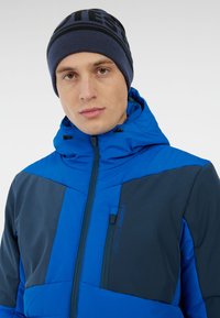 Modrá kapucňová bunda s vycpanými částmi v tmavě modré a světle modré barvě; obsahuje kapsu na zip a logo na prsou.