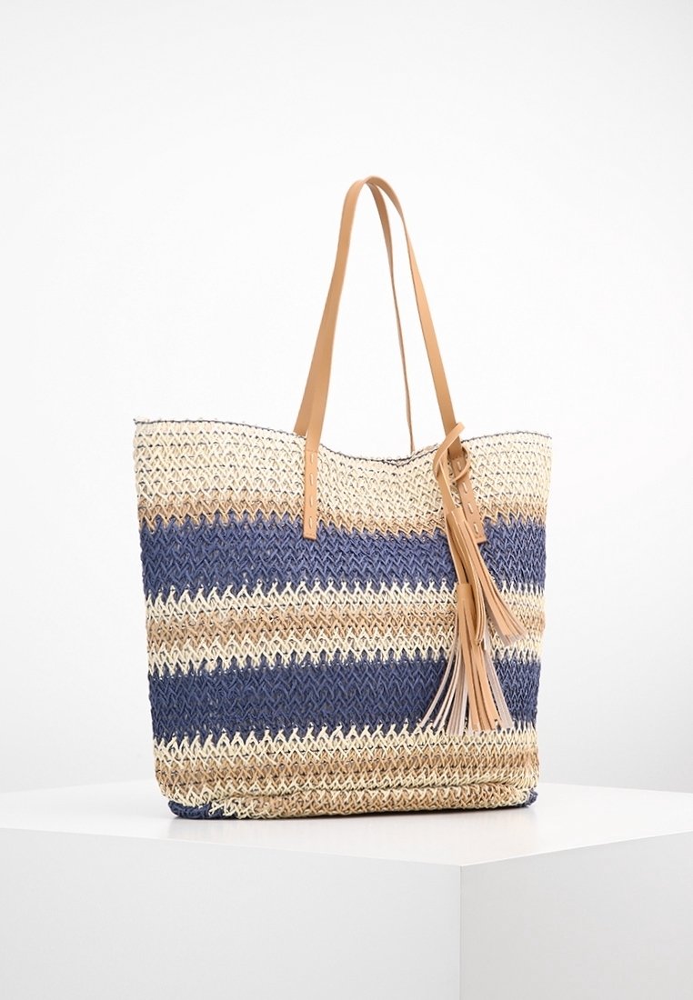 Sac cabas tissé avec des rayures horizontales bleues, beige et crème, poignées en cuir camel et détail pompon en cuir assorti.