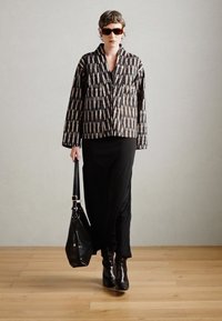 Jachetă cu motive negre, cu o croială lejeră, fustă lungă neagră, geantă robustă neagră și cizme negre până la glezne. Modelul poartă ochelari de soare închiși la culoare.