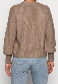 Pull marron en maille avec un tissage texturé, col rond et manches légèrement bouffantes, assorti à un jean en denim bleu clair.