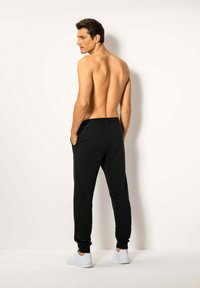 Schwarze Jogginghose mit elastischem Bund, seitlichen Taschen und schmalen Bündchen, kombiniert mit weißen Turnschuhen, Modell von hinten betrachtet.