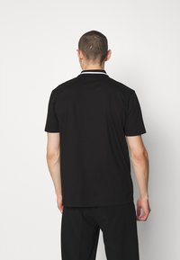 Černé polo tričko s krátkým rukávem, s klasickým límečkem a bílým lemováním. Vyrobeno z hladkého materiálu, minimalistický design bez viditelných log.