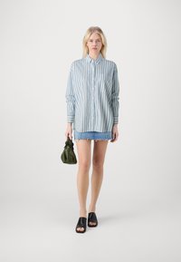 Light blue and white striped button-up shirt, denim mini skirt with frayed hem, black slide sandals, and green pouch handbag.