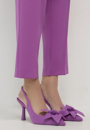 Escarpins slingback violets à bout pointu avec un grand détail de fleur en tissu, portés avec un pantalon raccourci assorti.