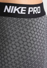 Legginsy Nike Pro mają czarny pas z białym logo oraz szary materiał w wzór nakładających się okręgów, zapewniając gładką i elastyczną teksturę.