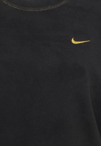 Schwarzer Fleecepullover mit rundem Halsausschnitt und goldgesticktem Nike-Logo auf der linken Brust. Weiche Textur mit sichtbaren Nähten.