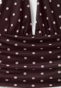 Gros plan sur un tissu rouge foncé avec des pois rose clair et un décolleté en V profond avec un assemblage froncé en dessous.