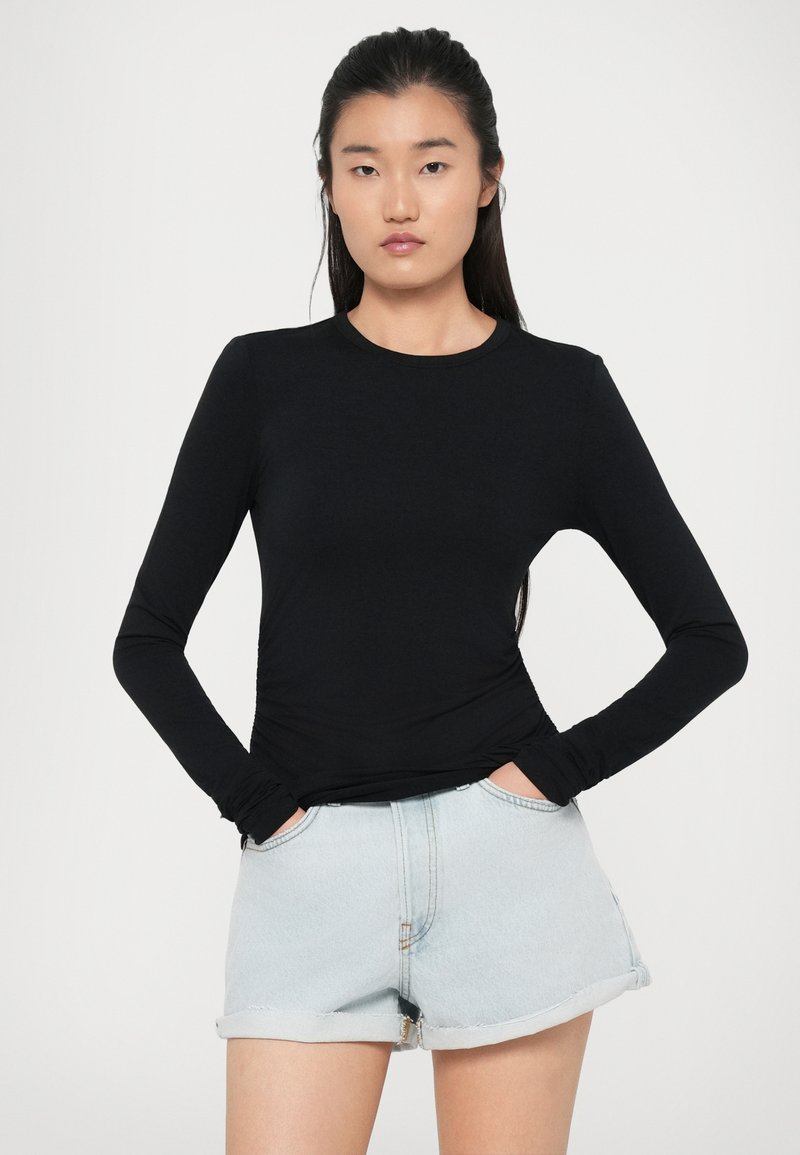 Zwarte langslavige top van rekbare stof, met een klassieke ronde hals en een aansluitend design. Gecombineerd met lichte denim shorts.