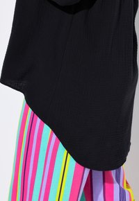 Top nero testurizzato con orlo arrotondato abbinato a pantaloni colorati a righe con linee verticali pink, teal, viola e giallo.
