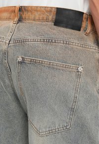 Vervaagde lichtgrijze denim jeans met een bruine label op de tailleband, voorzien van twee achterzakken en contrasterende stikseldetails.