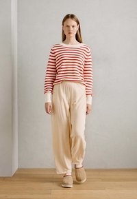 Rood en wit gestreepte gebreide trui met lange mouwen, gecombineerd met beige, losse broeken en beige instappers met rode accenten.