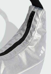 Scarpa sportiva argento con una superficie liscia e lucida, caratterizzata da una cerniera nera e un accento con logo bianco sul lato.