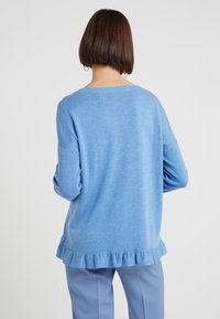 Pull bleu clair avec une texture douce, un large col et un ourlet à volants. Il présente des manches longues et une coupe décontractée, vu de dos.