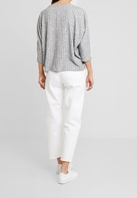 Maglietta grigia oversize con texture e maniche a tre quarti abbinata a pantaloni bianchi cropped e sneakers bianche, che mostrano una vestibilità rilassata.