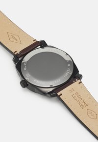 Schwarze Edelstahl-Uhr mit einem glatten grauen Zifferblatt, braunem Lederarmband und geprägtem "FOSSIL"-Logo; wasserdicht bis 5 ATM.