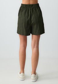 Shorts vert kaki avec des rayures verticales, fabriqués en tissu léger, dotés d'une taille élastique et de poches latérales.